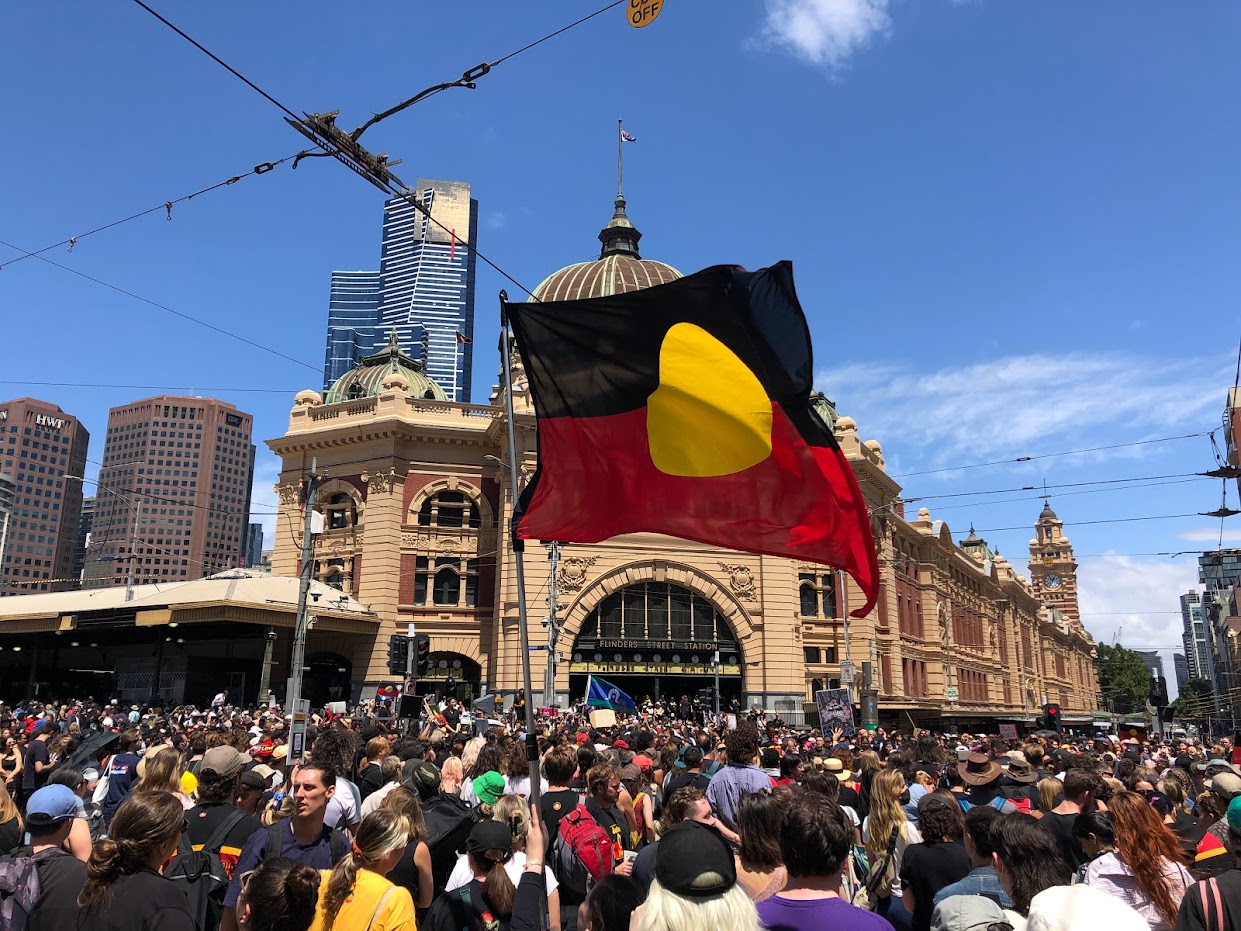 An Aboriginal flag flies amid the crowd outside Flinders Street Station during the Invasion Day rally in 2023